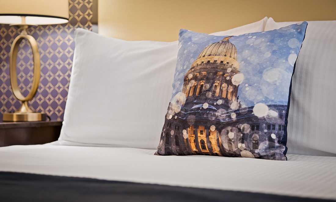Decorative pillow on a hotel room bed showing the Wisconsin State Capitol in Downtown Madison WI